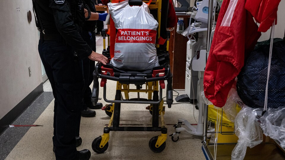 Un technicien ambulancier paramédical pousse une civière sur laquelle se trouve un sac contenant les effets personnels d'un patient. 