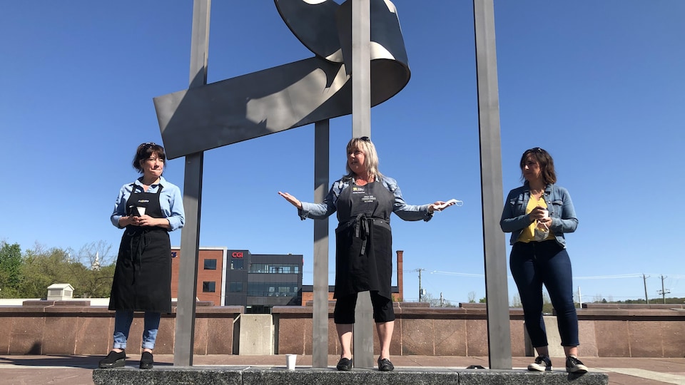 Trois femmes debout devant une sculpture.