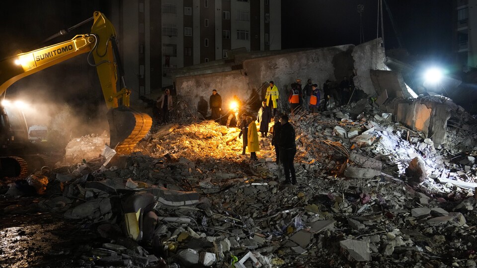 Des secouristes et de la machinerie dans des décombres à la tombée de la nuit.