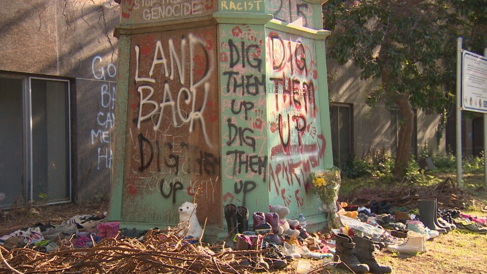 Des graffitis sur une statue et de nombreuses paires de chaussures à son pied.