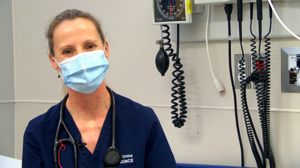 Une médecin qui porte un stéthoscope sourit sous son masque.