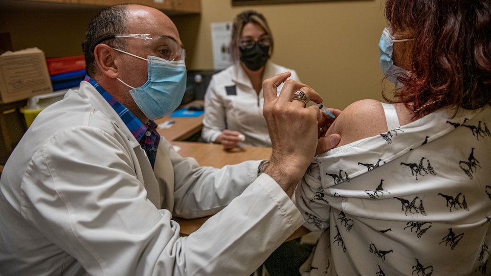 Un pharmacien vaccine une cliente contre la COVID-19