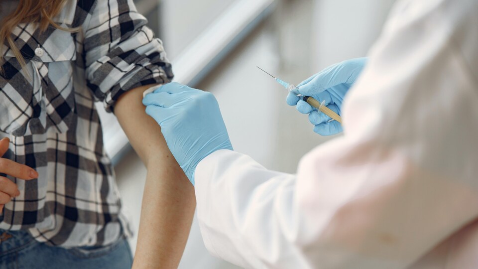 Une personne qui tient un vaccin et qui frotte le bras d'une femme avec une lingette désinfectante.