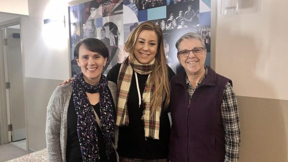 Trois femmes sont debout et sourient en regardant la caméra.