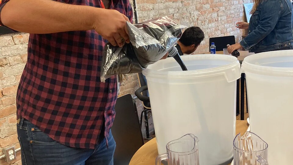 Un homme prépare du vin dans un baril de plastique.