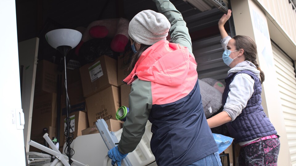 Deux bénévoles de l'organisme Shelter Movers ouvrent les portes d'un entrepôt rempli des meubles et objets appartenant à une femme victime de violence conjugale qui doit quitter son foyer.