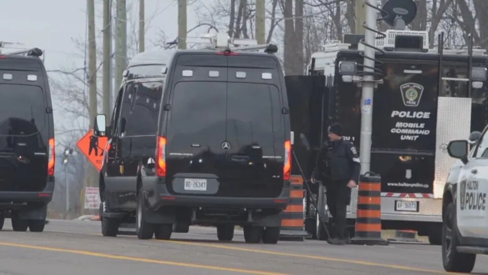 Des camions de police au bord d'une route.