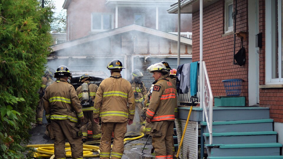 Une dizaine de pompiers éteignent une voiture en feu devant un garage. 