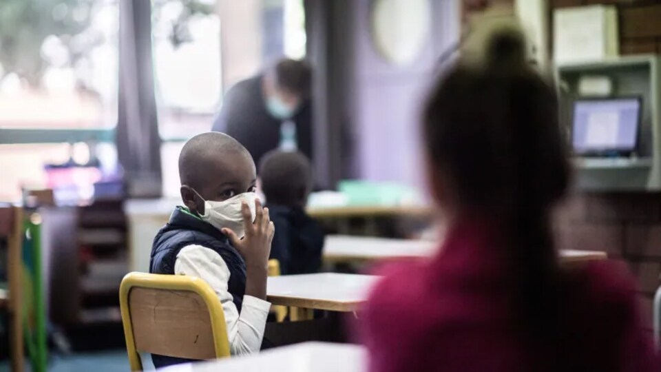 Un élève portant un masque se retourne vers un autre élève dans une salle de classe.