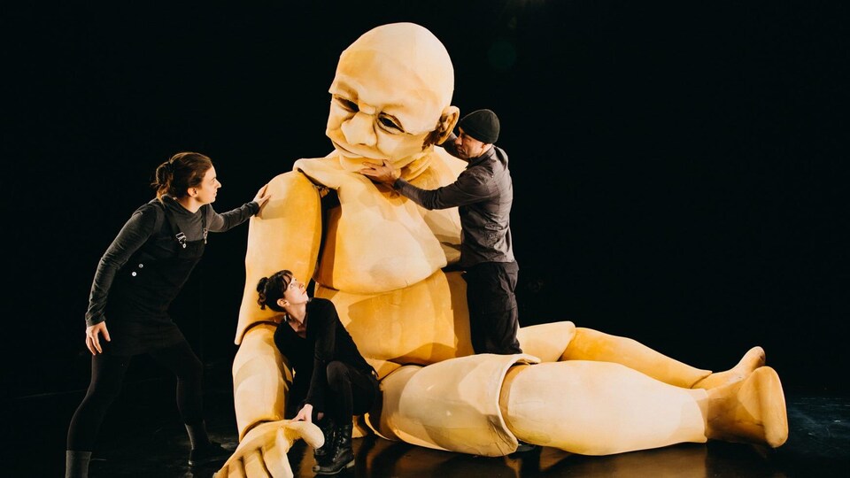 Trois personnes sur une scène de théâtre avec une marionnette géante.