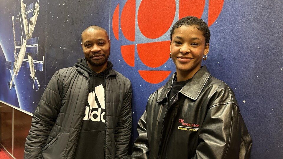 David Muipatayi et Julianne Lavertu sourient à la caméra. En arrière plan, le logo rouge de Radio-Canada.