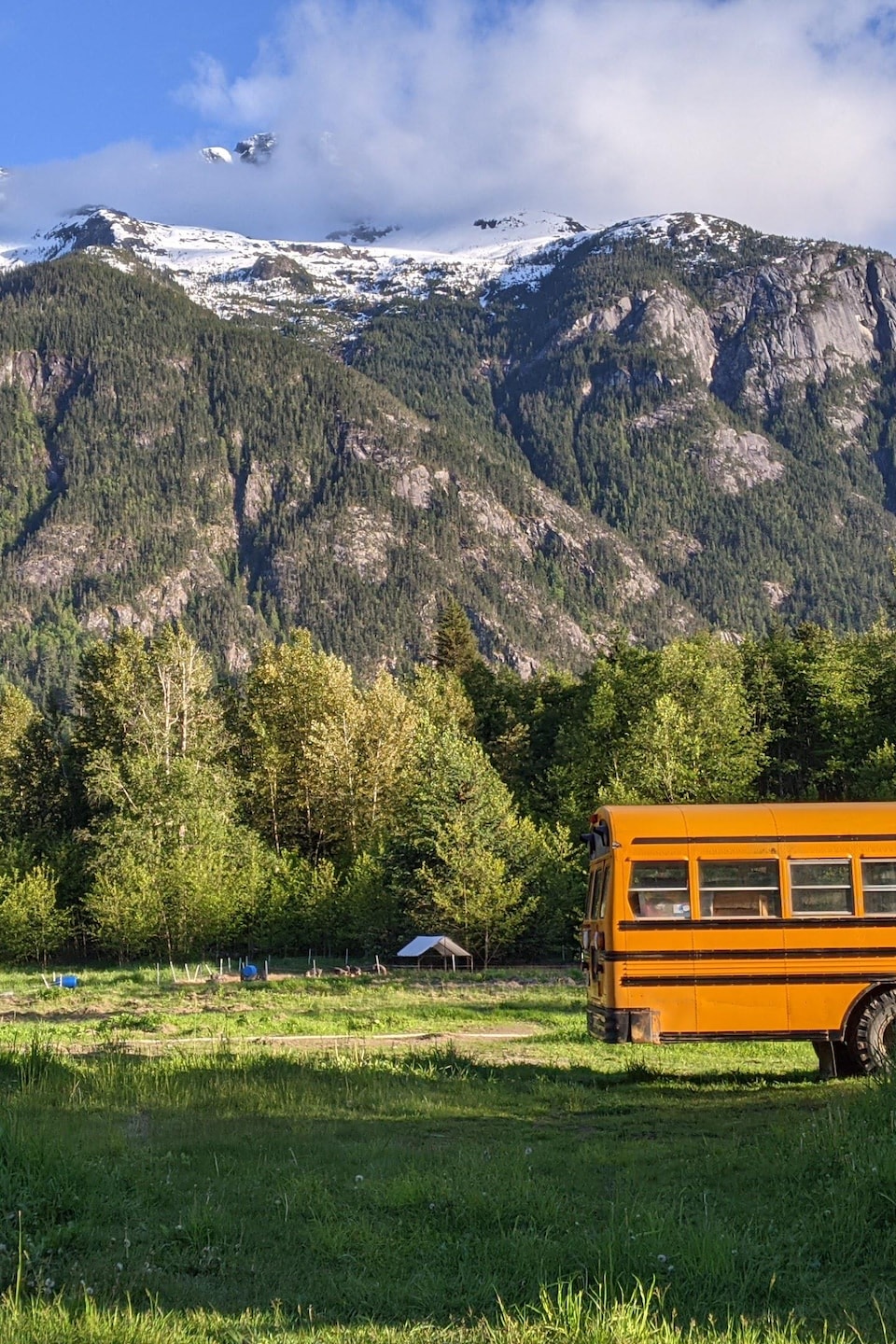 Ferme avec de vieux batiments, un vieux bus scolaire et les montagnes en arrière plan.