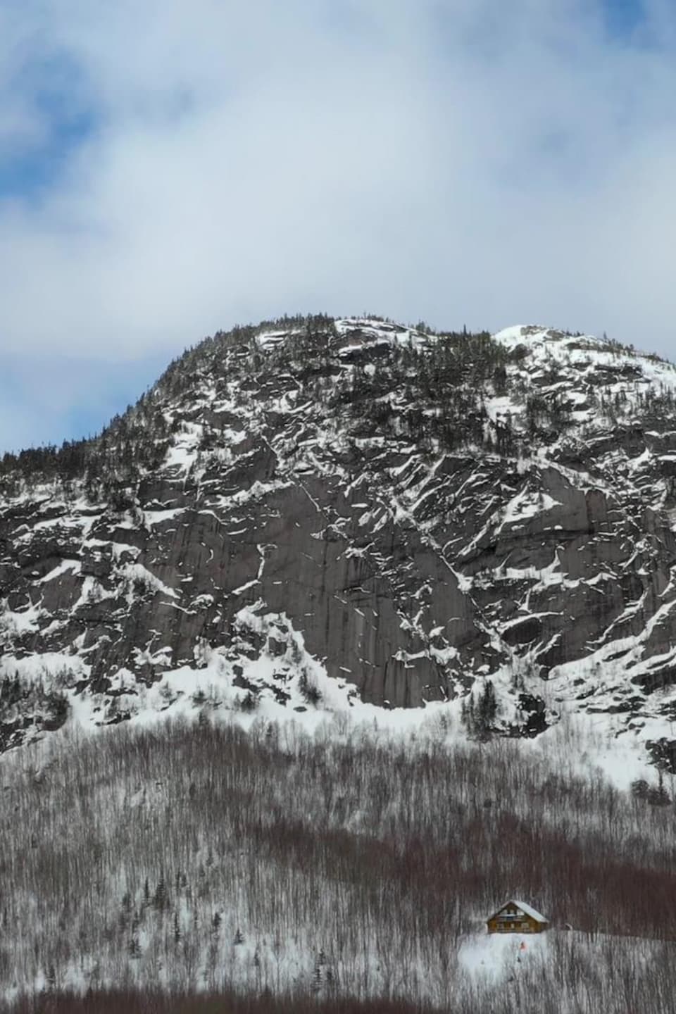 Une montagne enneigée avec au pied un chalet.