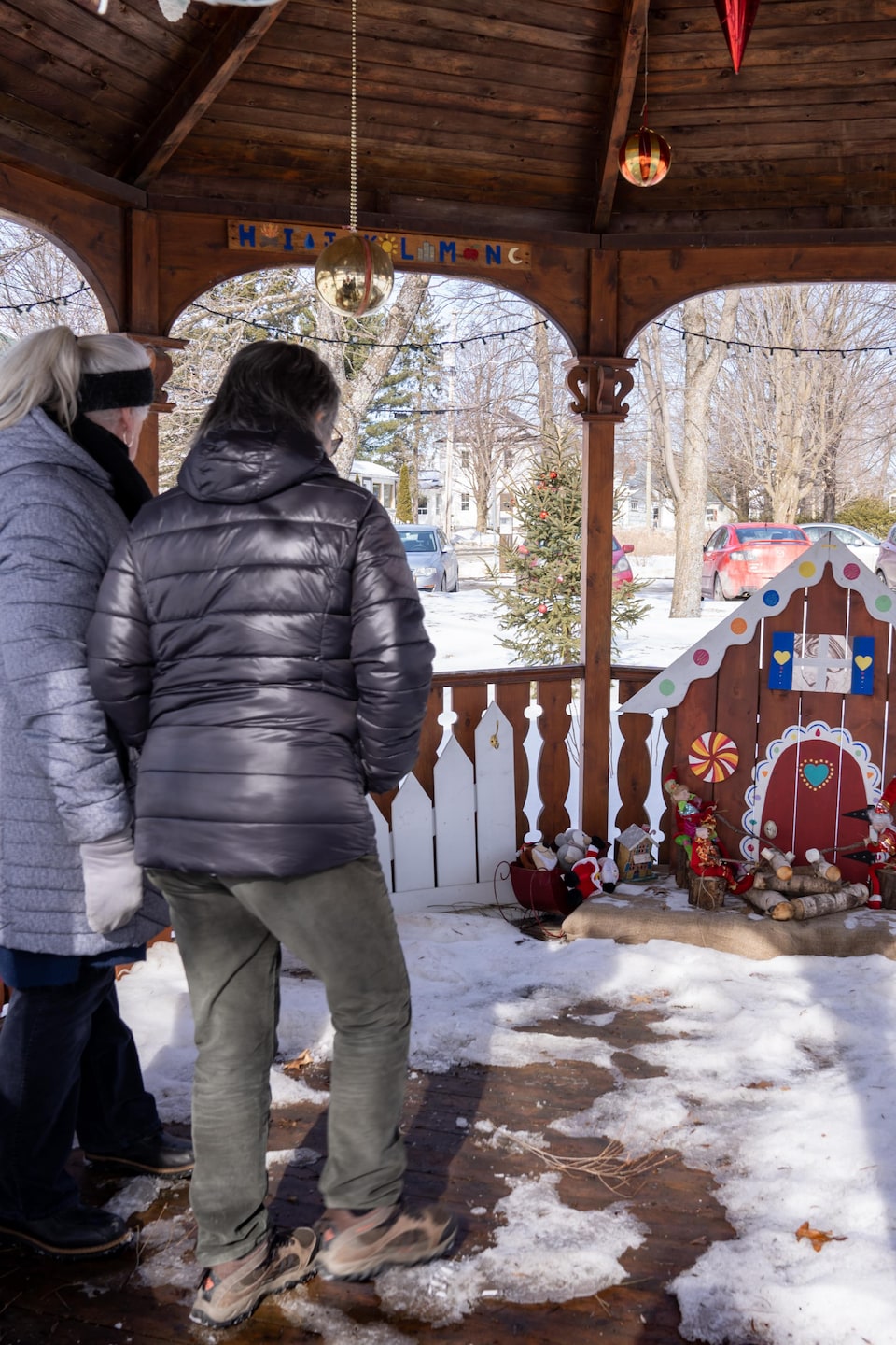 Deux dames regardent une crèche de Noël dans un kiosque extérieur en bois. 