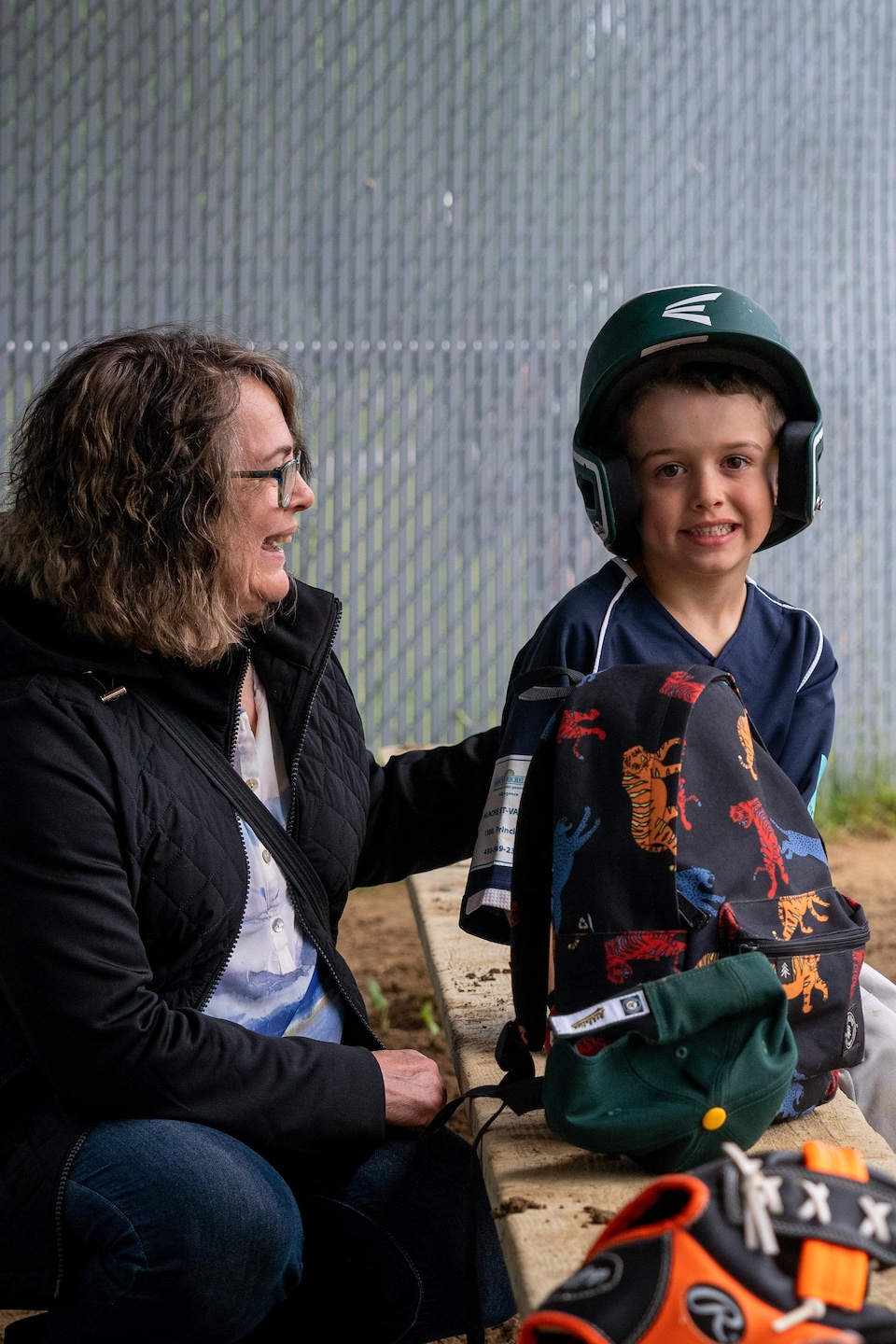 Une maman accompagne son fils sous un abri de joueurs de baseball.