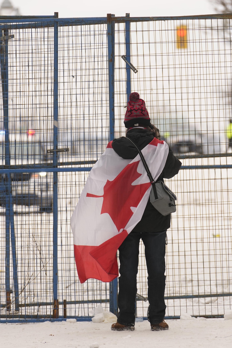Un homme drapé d'un drapeau canadien se tient devant une clôture temporaire au centre-ville d'Ottawa le dimanche 20 février 2022.