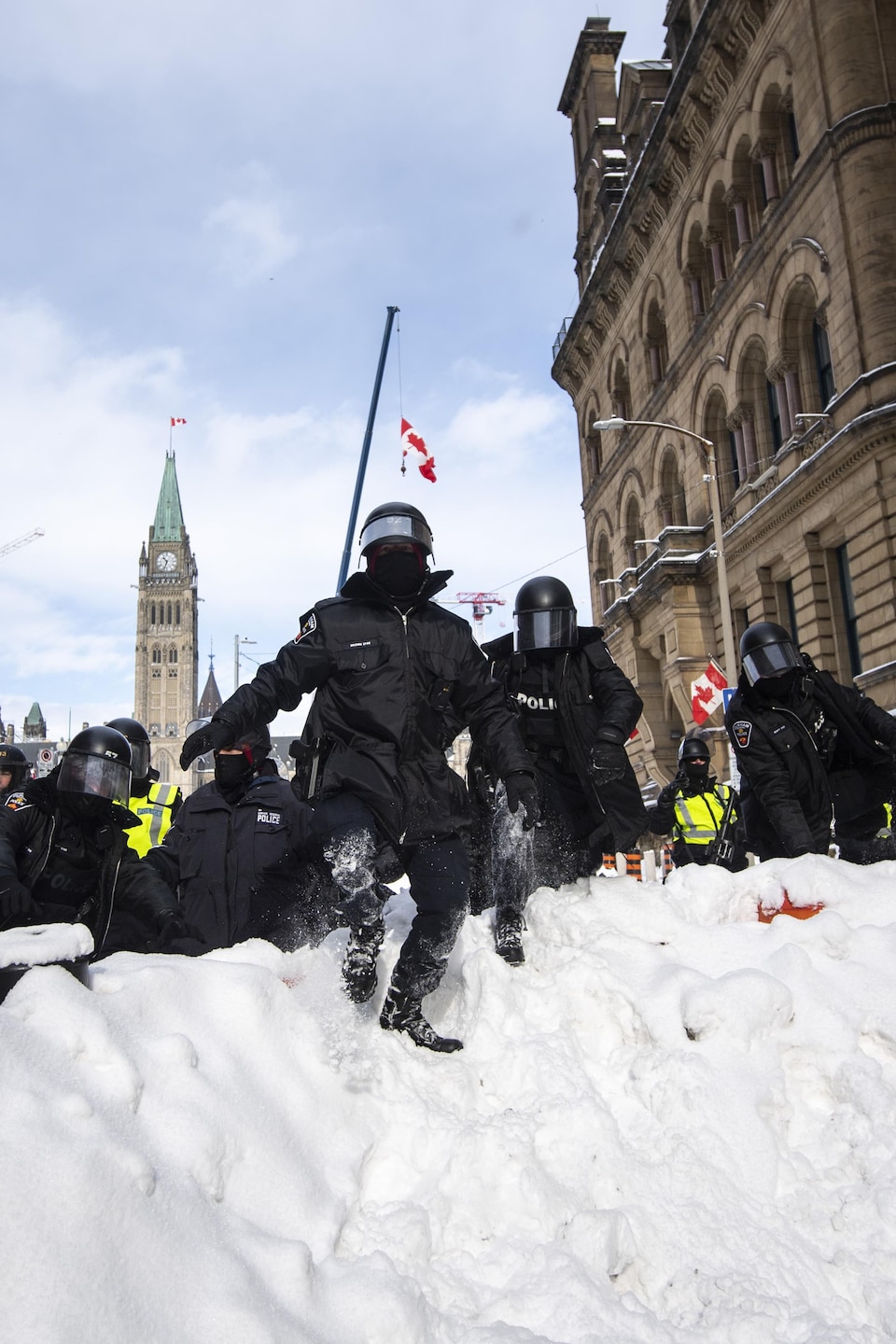 Un policier grimpe sur un banc de neige construit par des manifestants, alors qu'ils se déplacent pour dégager le centre-ville d'Ottawa près de la colline du Parlement après des semaines de manifestations, le samedi 19 février 2022. 