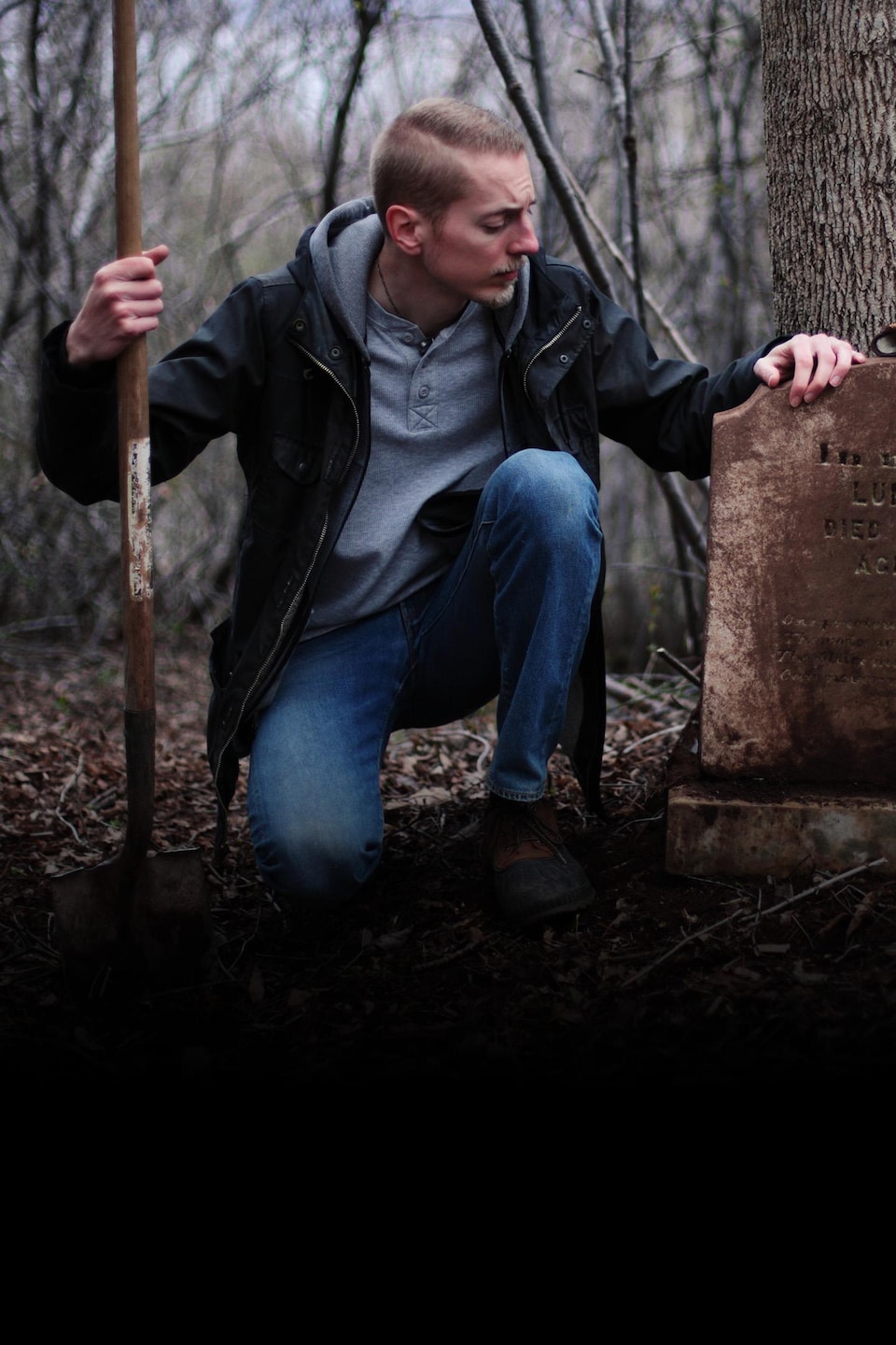 Steve Skafte est accroupi près d'une pierre tombale. Il tient une pelle de son autre main.