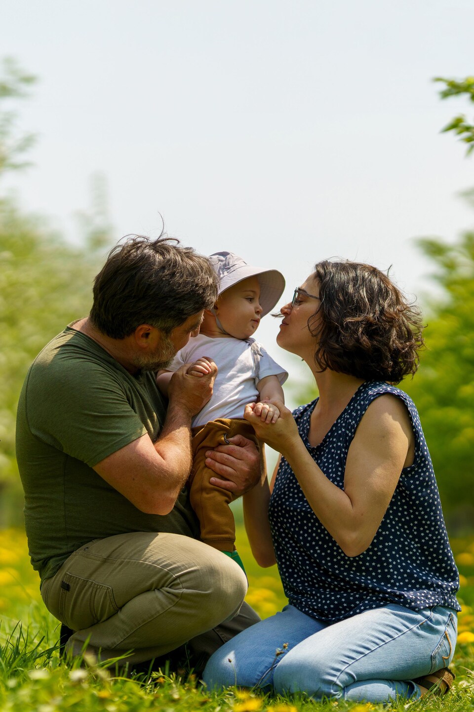 Un homme et une femme accroupis tenant un enfant dans leur bras au milieu d'un verger.