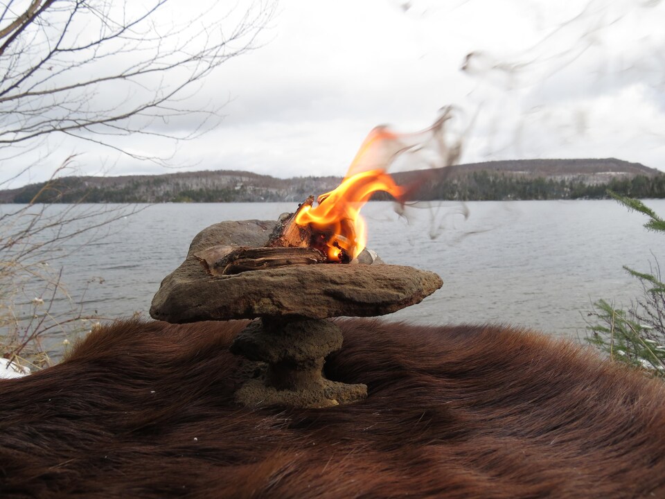 Des bouts d'écorce de bois en train de bruler sur une pierre.