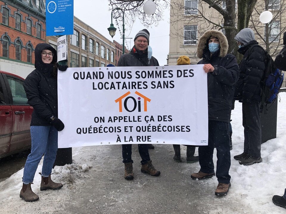 Des manifestants. Leur affiche dit "Quand nous sommes des locataires sans toit, on appelle ça des Québécois et des Québécoises à la rue". 