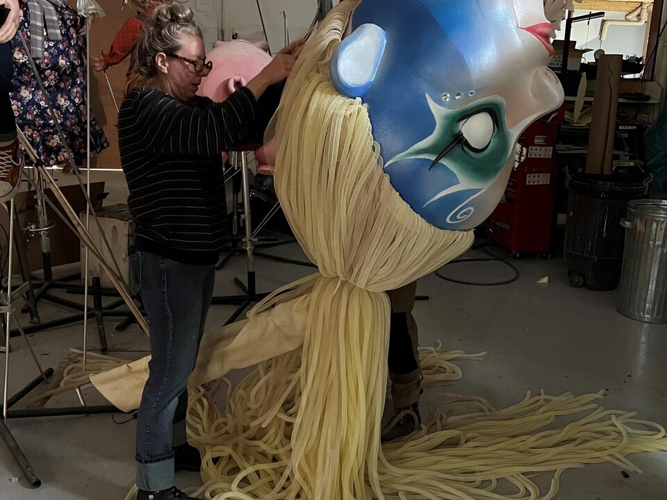 Une femme travaille sur la tête d'une marionnette géante. 