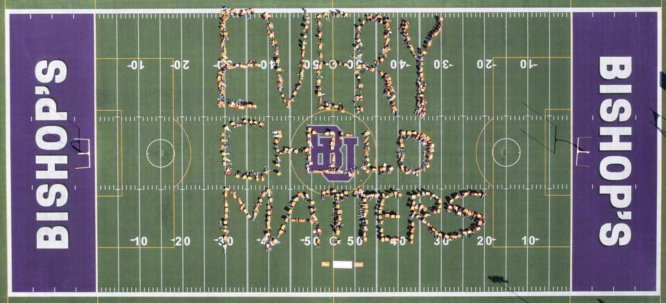 Un terrain de Football sur lequel des gens écrivent "Every child matters" avec leur corps. 