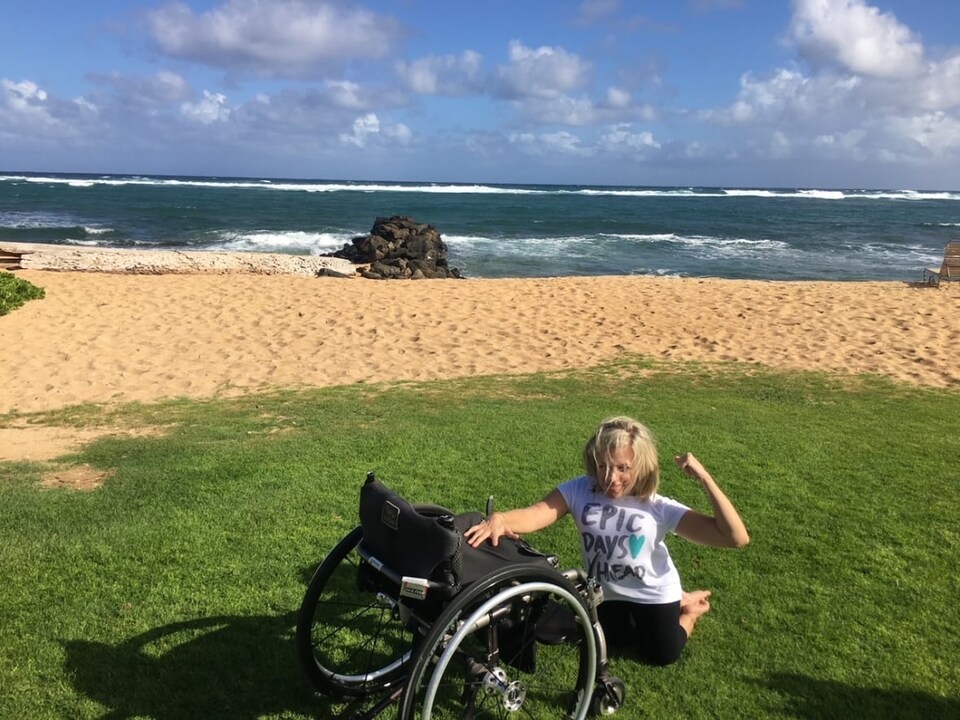 Kristina Hayes à côté de son fauteuil roulant sur une plage.
