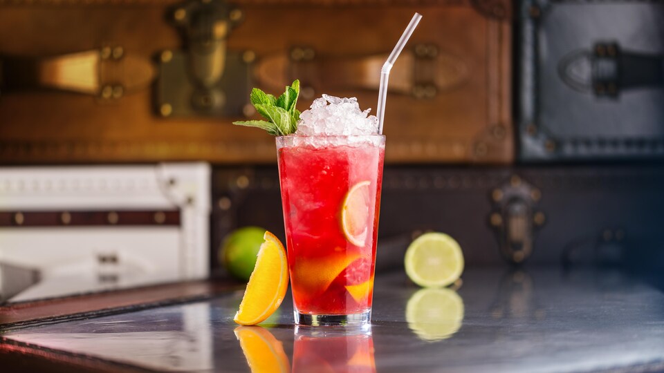 Un verre contenant un cocktail avec de la glace, une paille et des agrumes.