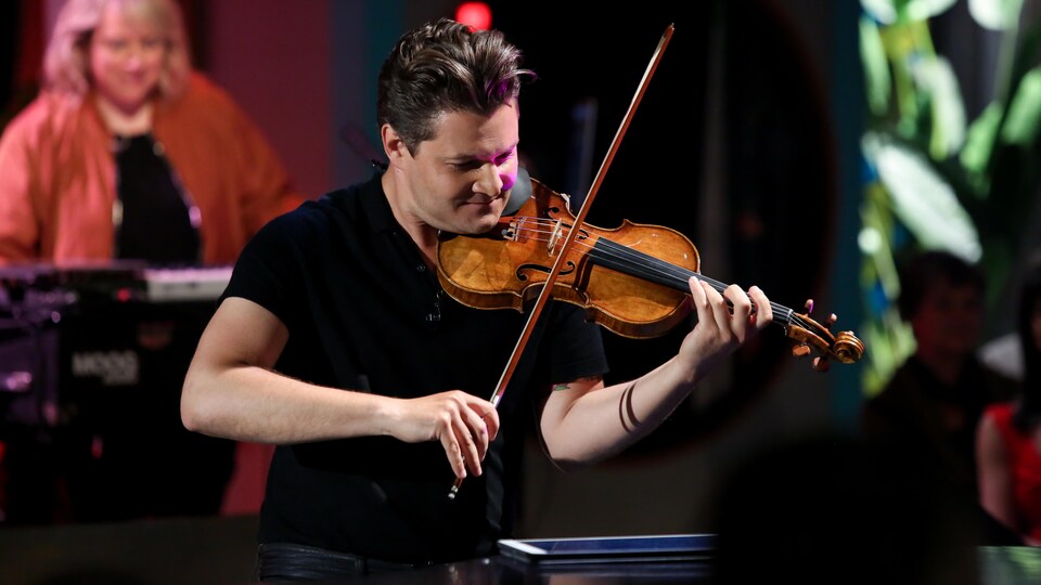 Un jeune homme portant un t-shirt noir joue du violon.