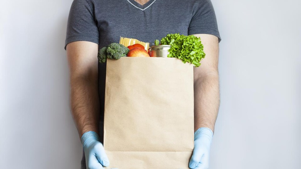 Un homme tient dans ses bras un sac d'épicerie.