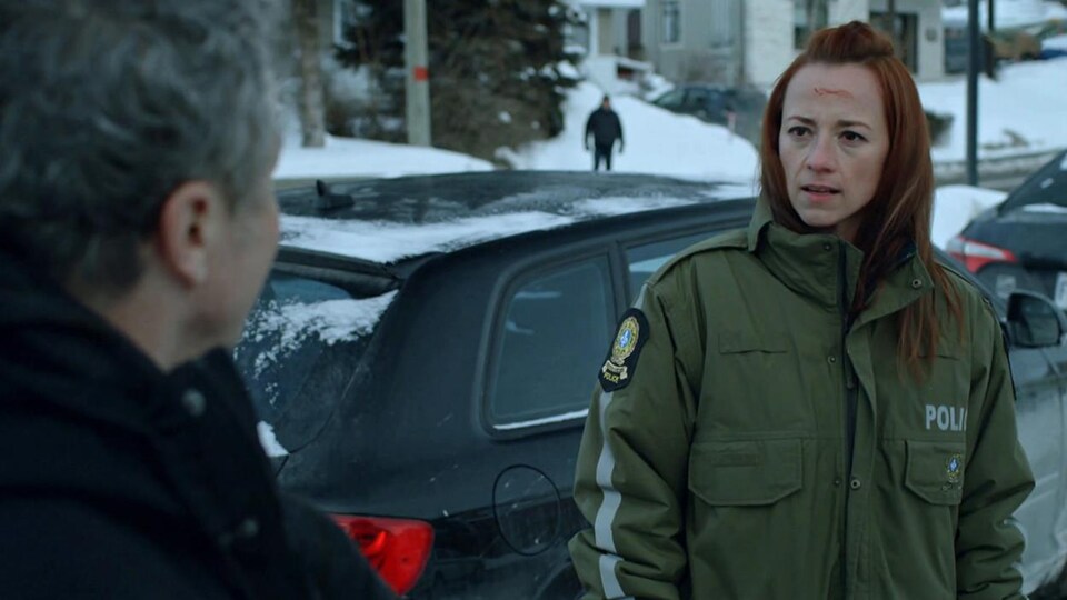 Une femme qui porte une veste de policière a du sang sur le front.