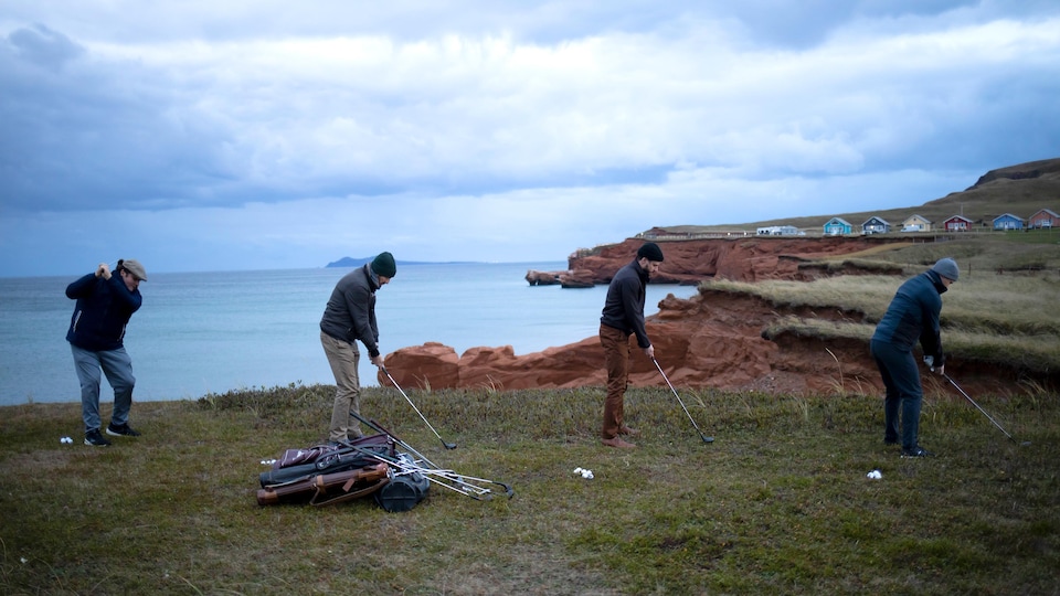Quatre hommes, de profil, jouent au golf devant une falaise.