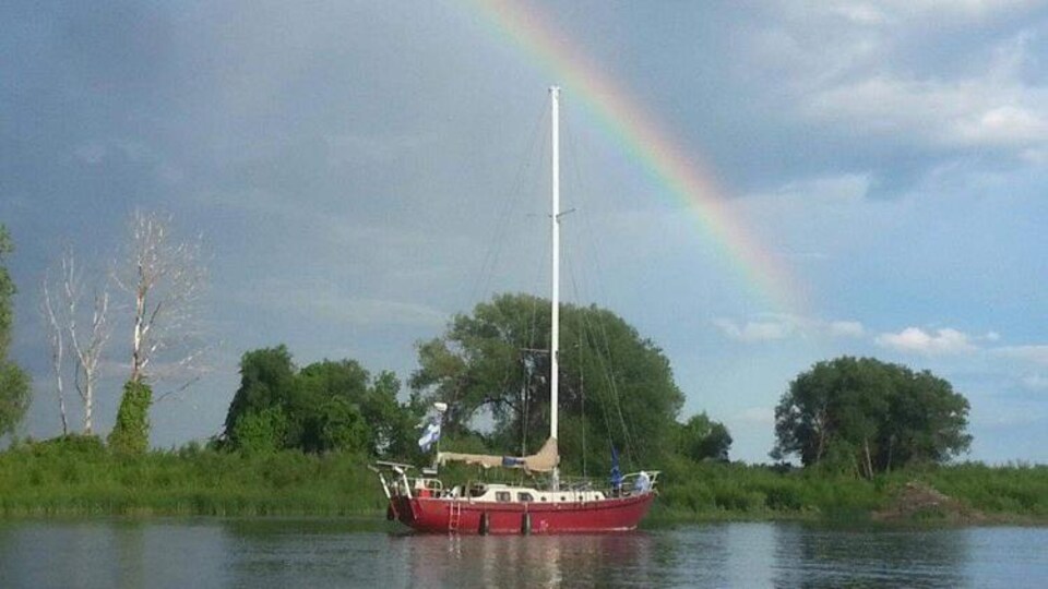 Un voilier sur le fleuve avec un arc-en-ciel.