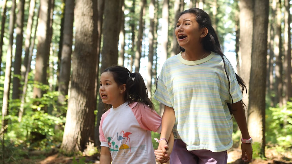 Une petite fille et une jeune fille, criant et se tenant par la main, courent dans un bois.