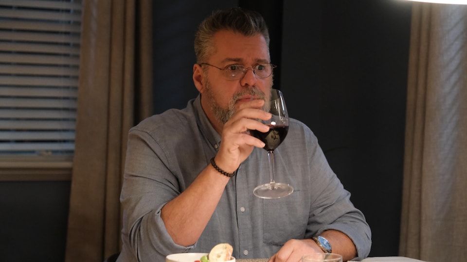 La personne est assise à une table avec un verre de vin à la main.