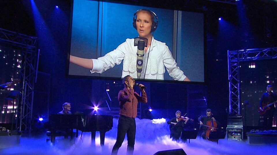 Céline est sur un écran et Pierre est sur scène accompagné par des musiciens.