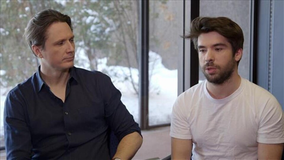 The director and the producer are in an interview, sitting near a window.