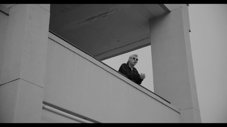 En noir et blanc, un homme à un balcon fume un cigare.