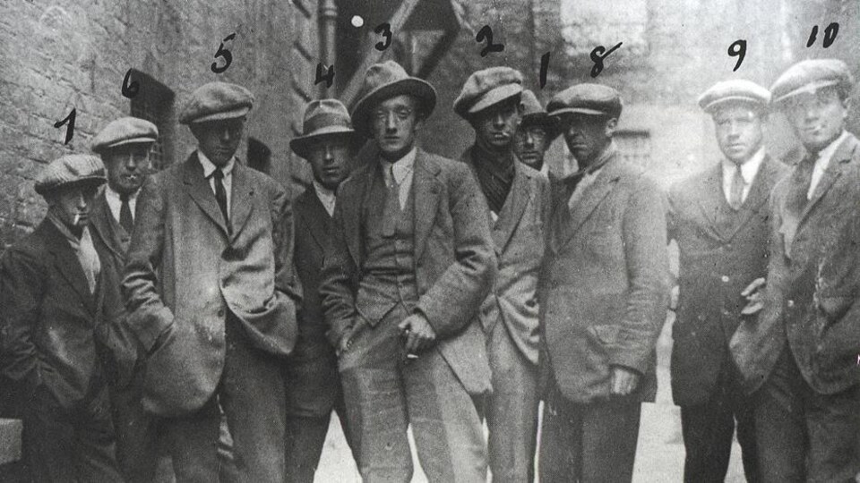 Dans une ruelle, 10 hommes en habits d'époque de 1920.