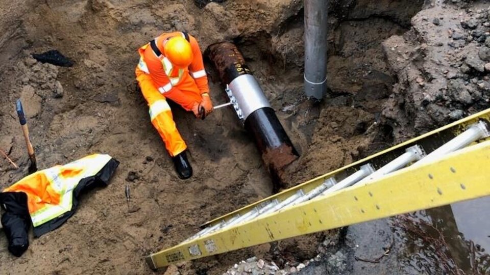 Un travailleur s'affaire à réparer une canalisation d'eau dans un trou.