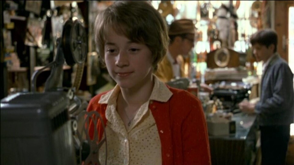 A shy and smiling girl looks at an old camera, in a store.