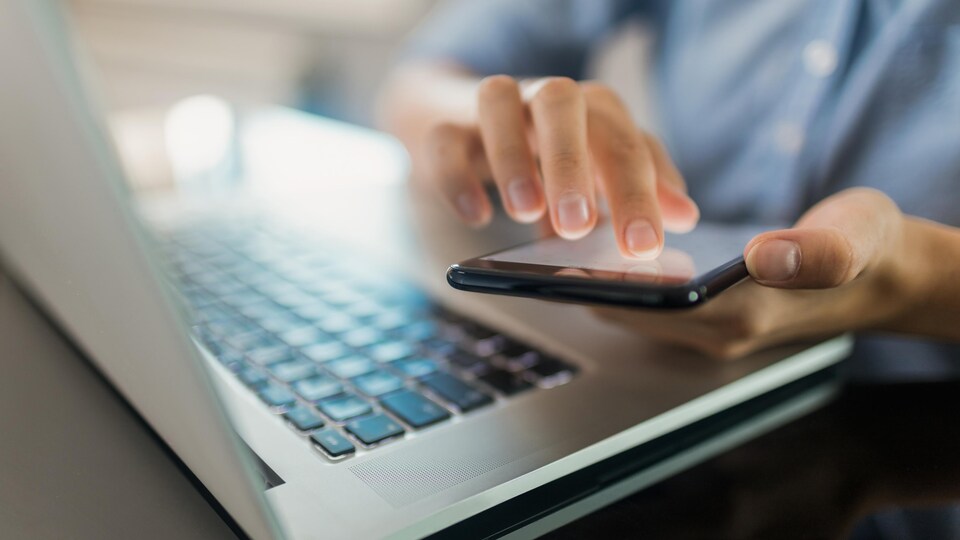 Une femme utilise un téléphone devant un clavier d'ordinateur portable.