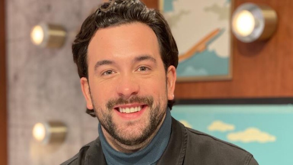Félix-Antoine Tremblay est sur le plateau d'On va se le dire. Il porte un chandail bleu et une veste kaki.