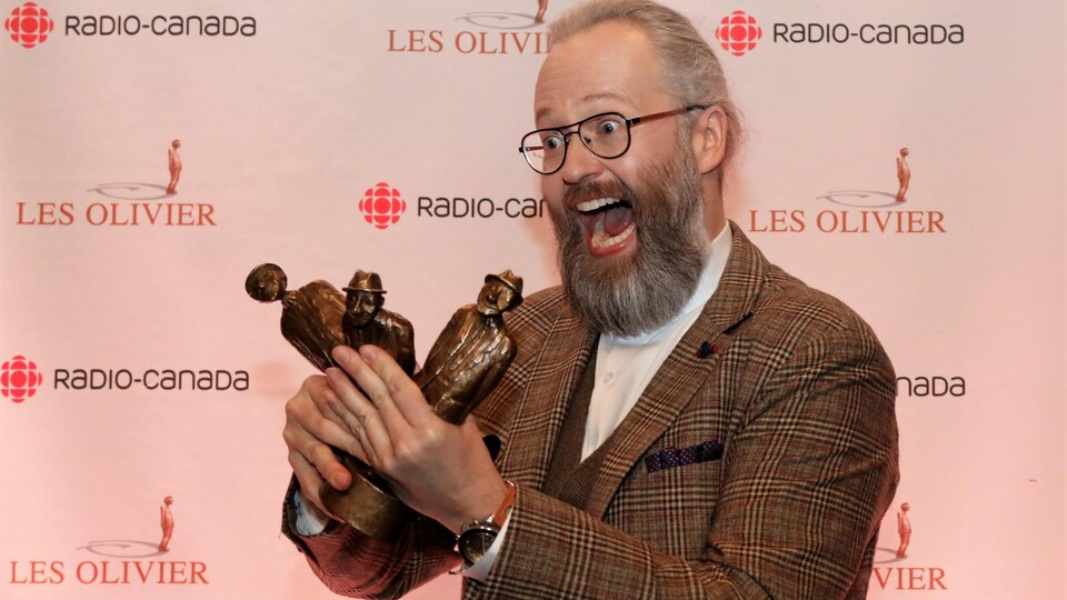 L'homme tient trois trophées Olivier dans ses mains.
