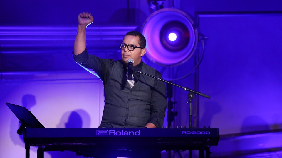 L'animateur est assis au piano le poing dans les airs.