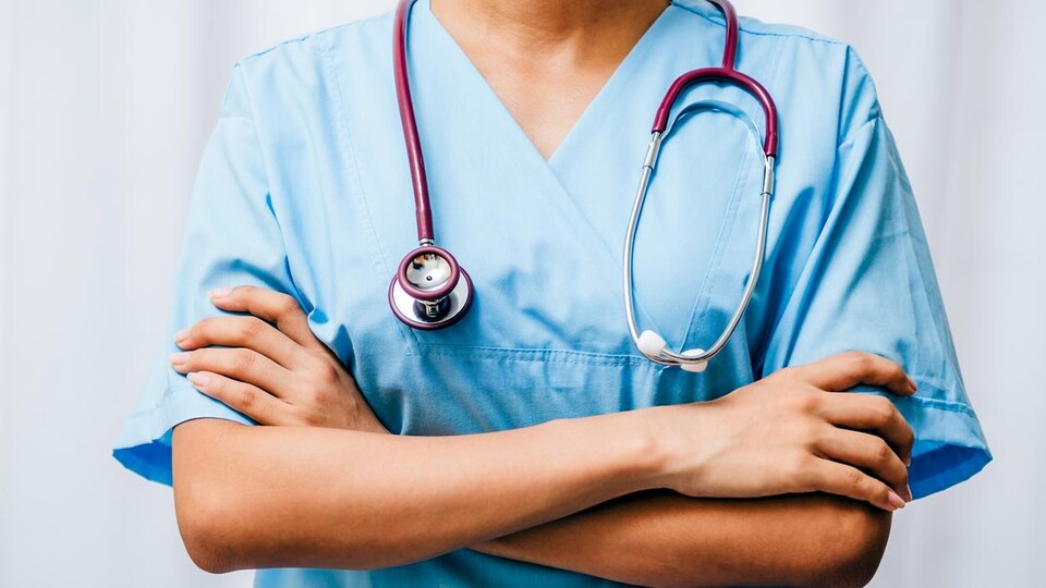 Un médecin qui porte un uniforme bleu. Son stéthoscope est dans son cou.