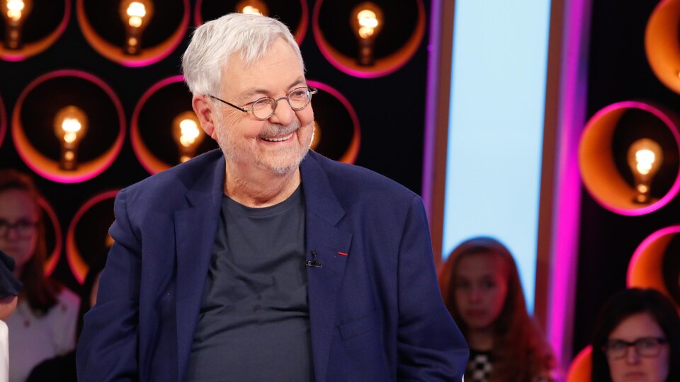 Michel porte un t-shirt et un veston bleus.