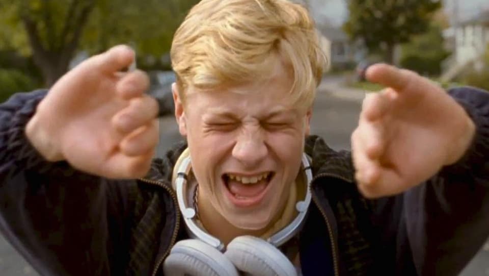 Un jeune homme blond, des écouteurs autour du cou, ouvre l'image de ses deux mains.