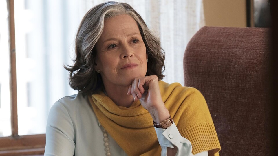Une femme (Sigourney Weaver) habillée chic, assise derrière un bureau.